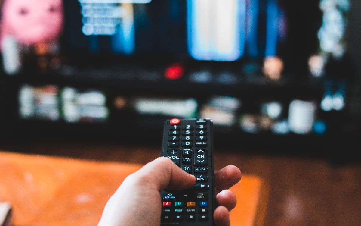 A hand holding a television remote in a living room